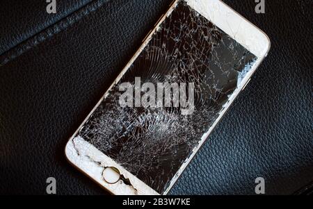 Modern smartphone with highly broken screen on black background. Stock Photo