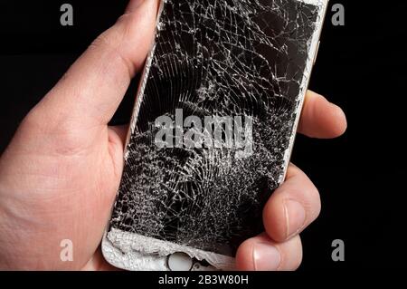 Modern smartphone with highly broken screen in men hand on black background. Stock Photo