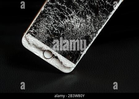 Modern smartphone with highly broken screen on black background. Stock Photo