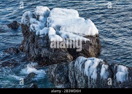 Rocks in the sea covered with ice from splashing waves, along the Avalon Peninsula in Newfoundland, Canada Stock Photo