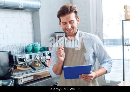 Young adult barista working in coffeeshop, making important notes in folder Stock Photo