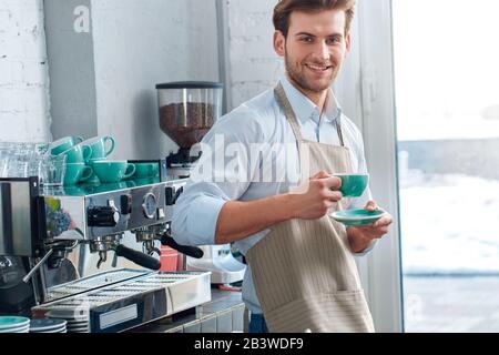 Coffee Passion. Young barista at coffee shop with cup of fresh hot expresso smiling happy Stock Photo
