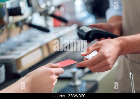 Young adult barista holding wireless terminal and taking card from client Stock Photo