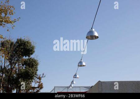 Round metallic lamps hanging between the square. Blue sky and trees in the background. Daylight Stock Photo