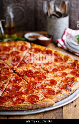 Large pepperoni pizza on wooden table in a rustic setting Stock Photo