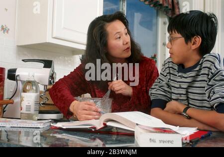 Austin Texas USA: Chinese mother and Chinese-American 13-year-old son review his homework in the kitchen. MR ©Bob Daemmrich Stock Photo