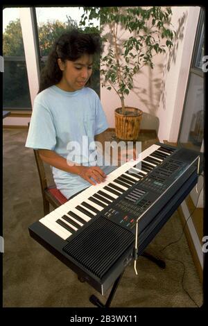 Austin Texas USA, circa 1990: Hispanic seventh grade girl practices playing electronic organ at her home. MR ©Bob Daemmrich Stock Photo