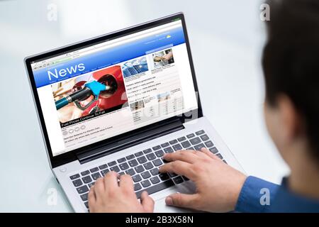 Close-up Of Businessperson Checking Online News On Laptop At Desk Stock Photo