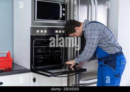 Male Technician In Overall Installing Oven In Kitchen Stock Photo