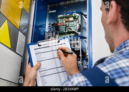 Cropped Image Of Male Electrician Holding Clipboard While Examining Fusebox Stock Photo