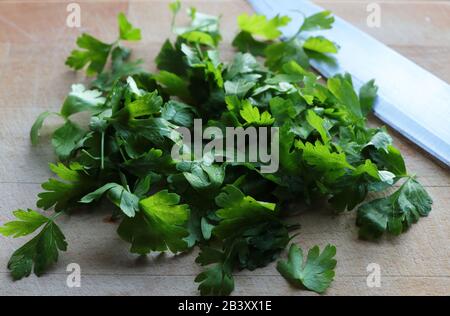 Parsley leaves on wood chopping board with large knife Stock Photo
