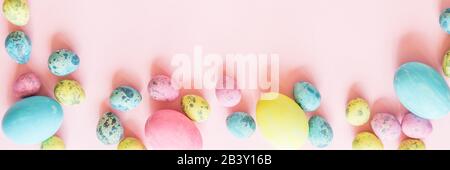 Stylish background with colorful easter eggs isolated on pink pastel background with blooming cherry branches. Horizontal long banner for web design Stock Photo