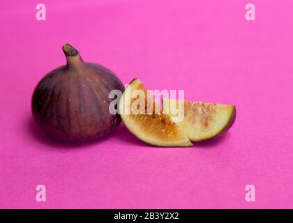 Two figs, one whole and one cut, lie on a bright pink background. Stock Photo