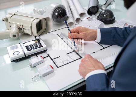 Architect Drawing Blueprint With Various Security Equipment On Desk Stock Photo