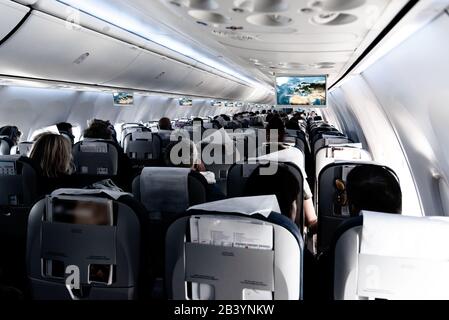 Commercial airplane passenger cabin view with unrecognizable travellers seated during flight. Travel concept. Stock Photo