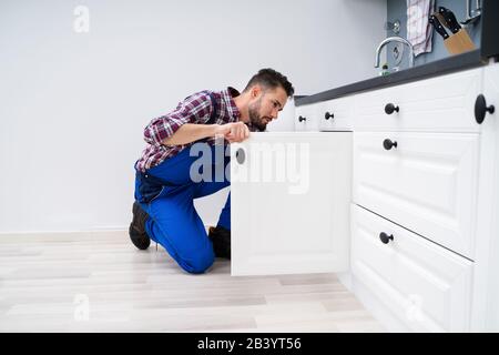 Young Handyman Fixing Sink Door In Kitchen Stock Photo