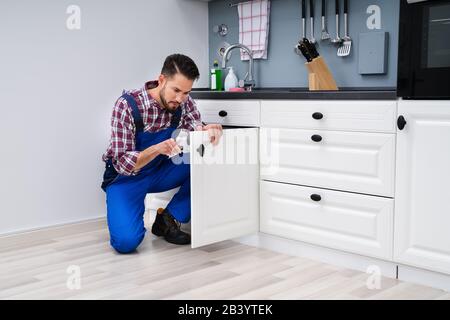 Young Handyman Fixing Sink Door In Kitchen Stock Photo