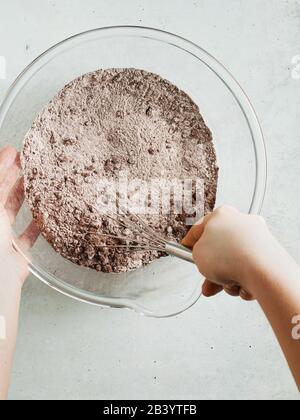 mixing dough for chocolate cake in a bowl. female hands and a kitchen whisk. recipe step by step Stock Photo