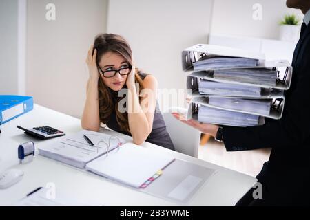 Businessman Giving Pile Of Folders To Female Assistant Stock Photo