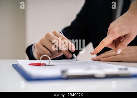Close-up Of A Person's Hand Signing Contract With Keys On It Stock Photo