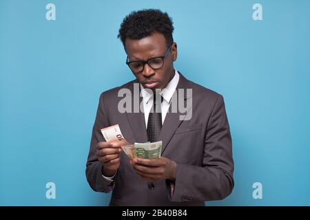 Serious african american business man counting money. Studio shot on blue wall. Stock Photo