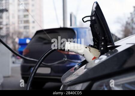 White plastic plug-in connector in the electric car. Car while charging battery. Ecological transportation. Side view. Stock Photo