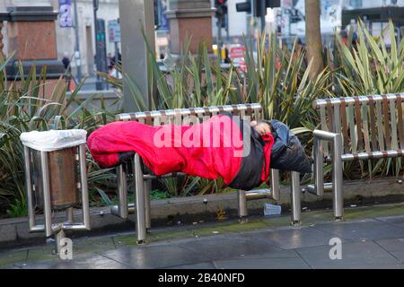 A homeless person asleep on a bench in Leeds City Centre Stock Photo
