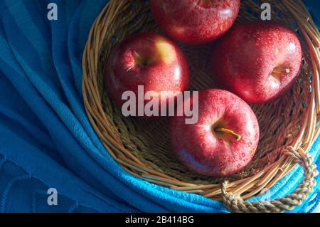 red apples in hand made basket with blue background Stock Photo