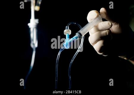 Nurse pushes IV medication by syringe into IV medication port with dark background. Stock Photo