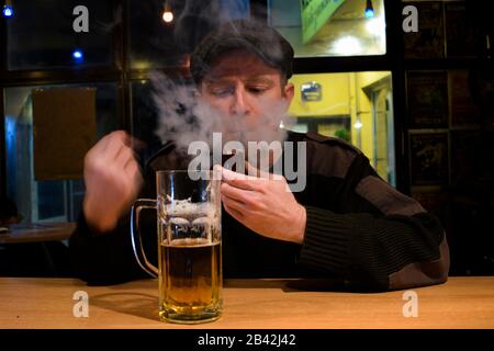 Red haired almost Irish guy seating in the bar and drinks some beer and smokes wooden pipe Stock Photo