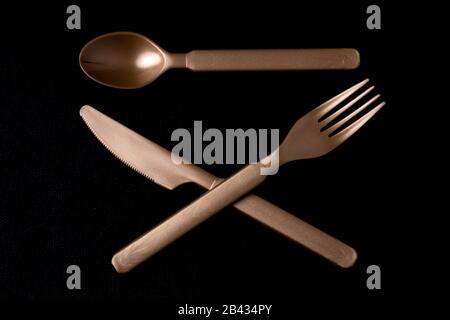 Shiny dark gold coloured plastic cutlery with a spoon above a crossed knife and fork Stock Photo