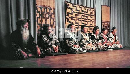 An old bearded chief and six elderly Ainu women rest before performing traditional Ainu dances, chants and hand-clapping to entertain Japanese tourists on the island of Hokkaido in northern Japan. Only 300 pure-blooded Ainu (pronounced I-noo) were still living when this historical photograph was taken in 1962. Since that time the Ainu have assimilated into Japanese society and their age-old way of life is only glimpsed today in special tourist villages. The Ainu were officially recognized as indigenous people of Japan in 2008. Stock Photo