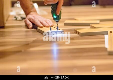 Wooden furniture assembling, woodworker screwing screws using a cordless Assembling furniture from chipboard, using a cordless screwdriver furniture Stock Photo
