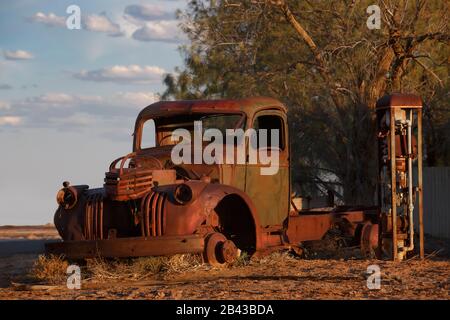 abandoned rusty old pick up truck wreck sits derelict on the side of a road on sunset Stock Photo