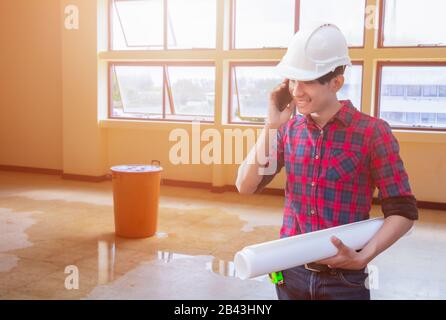 Engineer talk using cell phone and hand holding rolled blueprints with water leak drop interior office background Stock Photo