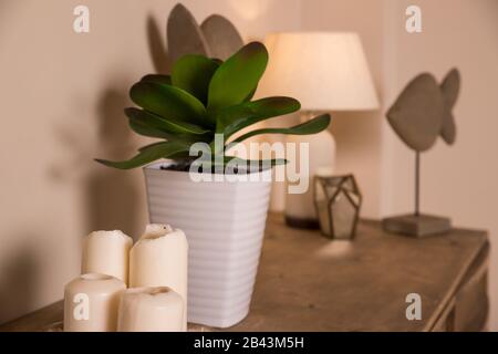 A white candles, lamp and a small potted plant are placed on the table in the bedroom.Candles, decor and green plant in white pot on the table in Stock Photo