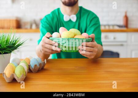 Happy Easter. A funny bearded man holds a basket with eggs and rabbit ears in the decorated room. Stock Photo