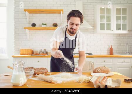 Baker male bearded man makes fresh bread dough at a table in the bakery kitchen. Stock Photo