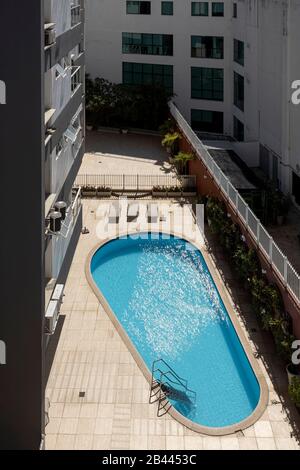 Empty swimming pool enclosed in urban surrounding part of a luxury apartment building in full sunlight Stock Photo