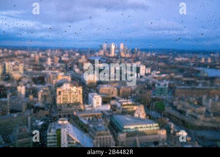 Raindrops on a window pane of glass with blurred background of River Thames and City of London Canary Wharf financial district Stock Photo