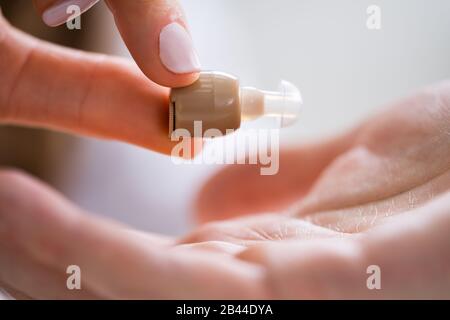 Cropped Image Of Female Doctor Giving Hearing Aid To Male Patient In Clinic Stock Photo