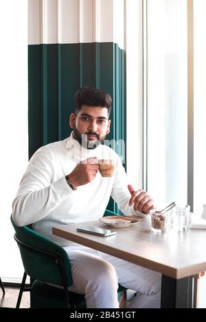 Young indian man drinking coffee in cafe and looking at camera. Stock Photo