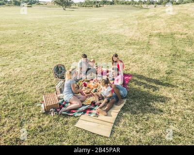 Happy families doing picnic in park outdoor - Young parents having fun with children in summer time eating and playing - Food, weekend lifestyle and f Stock Photo