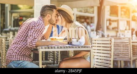 Happy travel couple kissing in bar restaurant for date dineer - Young lovers kissing having tender moments on summer vacation - Love, holidays, happin Stock Photo