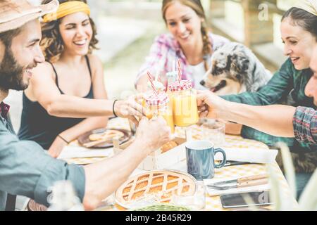 Happy millennial friends cheering at breakfast brunch meal in nature outdoor - Young people having fun together eating fruits and drinking smoothies - Stock Photo