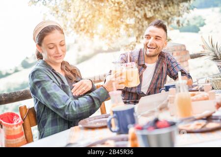 Happy couple doing breakfast meal in nature - Young people having fun with on weekend day eating fruits and drinking smoothies - Focus on man face - F Stock Photo