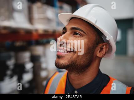 Side close-up of successful african american male worker looking away in warehouse wearing a white helmet Stock Photo