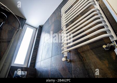 White contemporary electric towel dryer mounted on black tiled wall in modern bathroom. Stock Photo