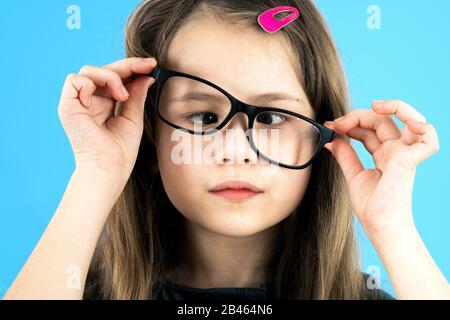 Close up portrait of a cross eyed child school girl wearing looking glasses isolated on blue background. Stock Photo