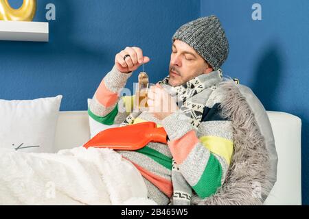 a man with a cold lies on the couch and drinks tea Stock Photo